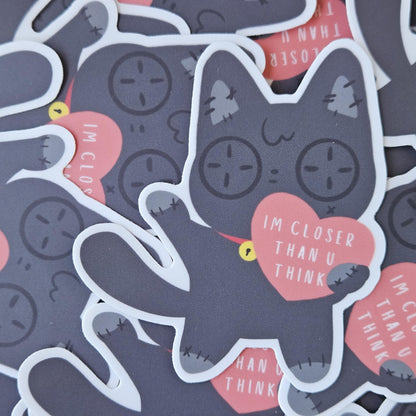Sticker with a cat design and text 'I'm closer than you think' on top of a grouping of the same stickers.