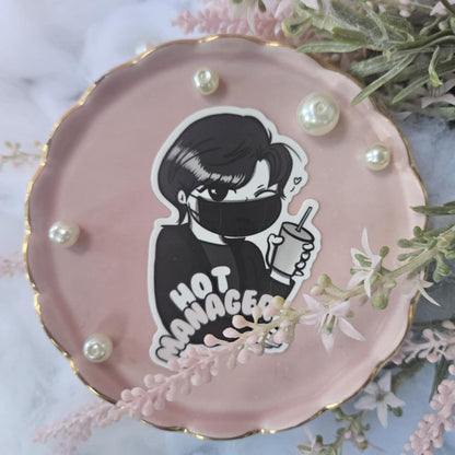Pink decorative plate with a sticker of a person wearing a mask and holding a drink, labeled 'Hot Manager', surrounded by decorative elements on a marble surface.