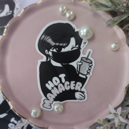 Pink round object with a black and white illustration of a person wearing a mask and 'HOT MANAGER' text, surrounded by pearls.